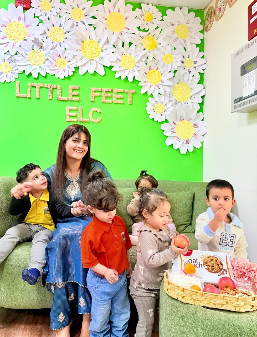 An educator with a group of children in front of the Little Feet flower wall
