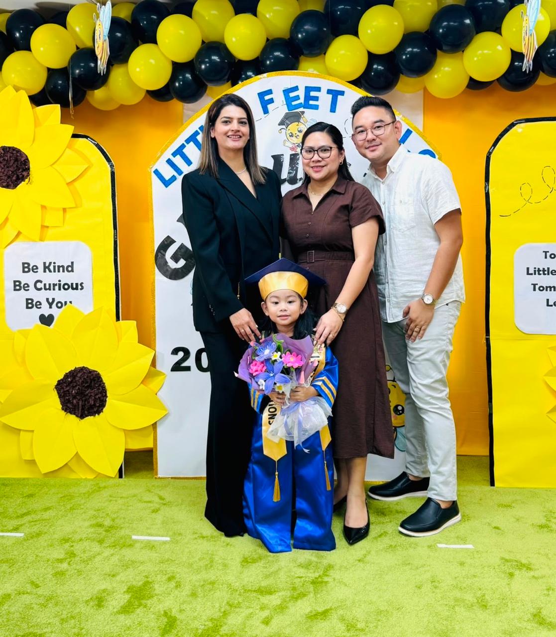 A graduate in cap and gown with her family and the nursery principal
