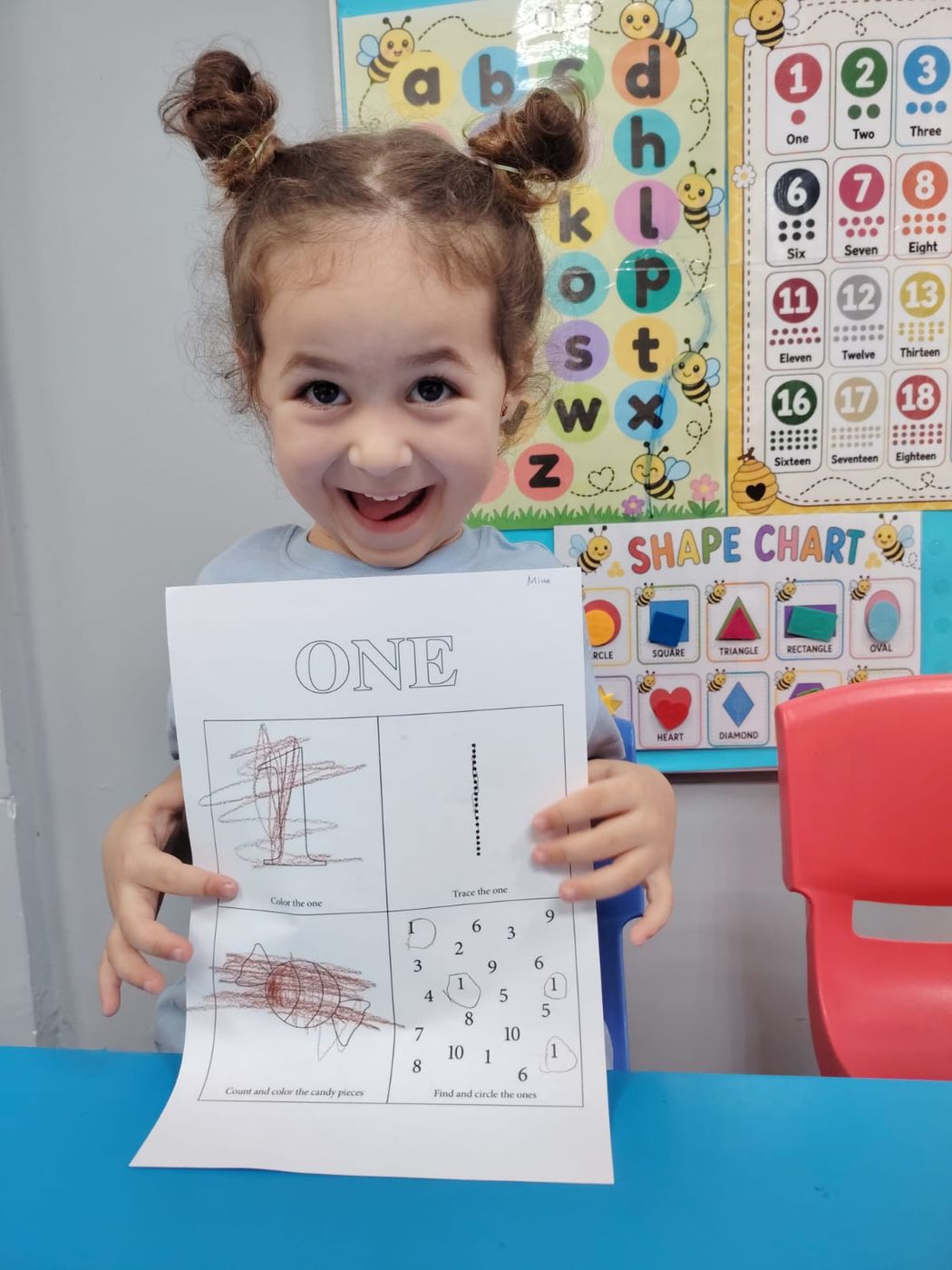 A smiling girl holding up her number one worksheet